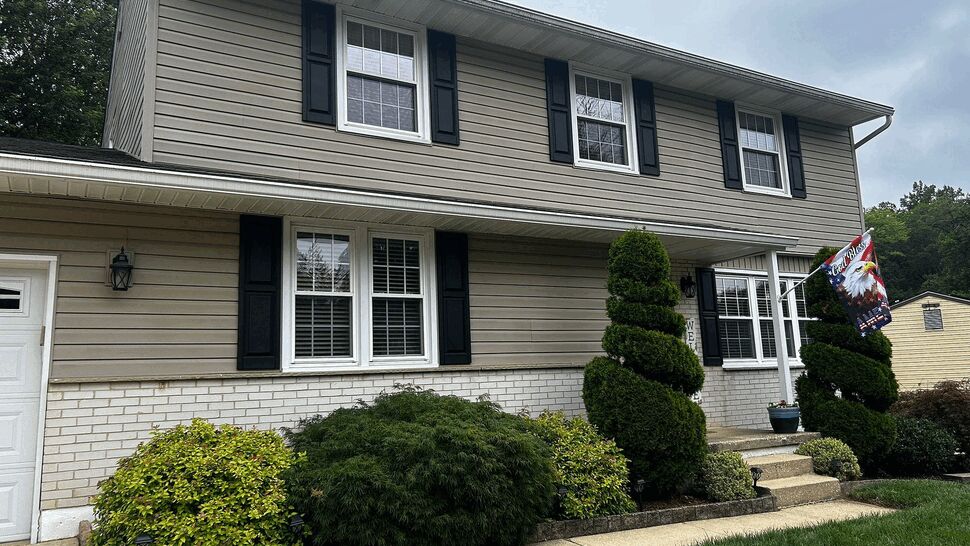 Two-story beige house with white brick and black shutters.