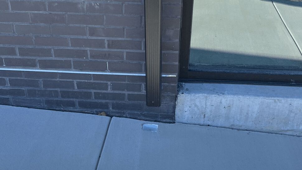 Black gutter downspout running down a brick wall beside a glass door