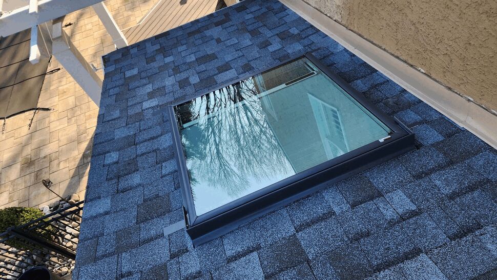 Square skylight installed on blue asphalt shingle roof.