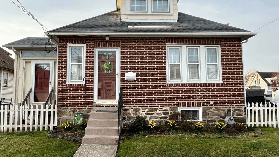 Front view of a brick bungalow with red door, white trim, and a picket fence.
