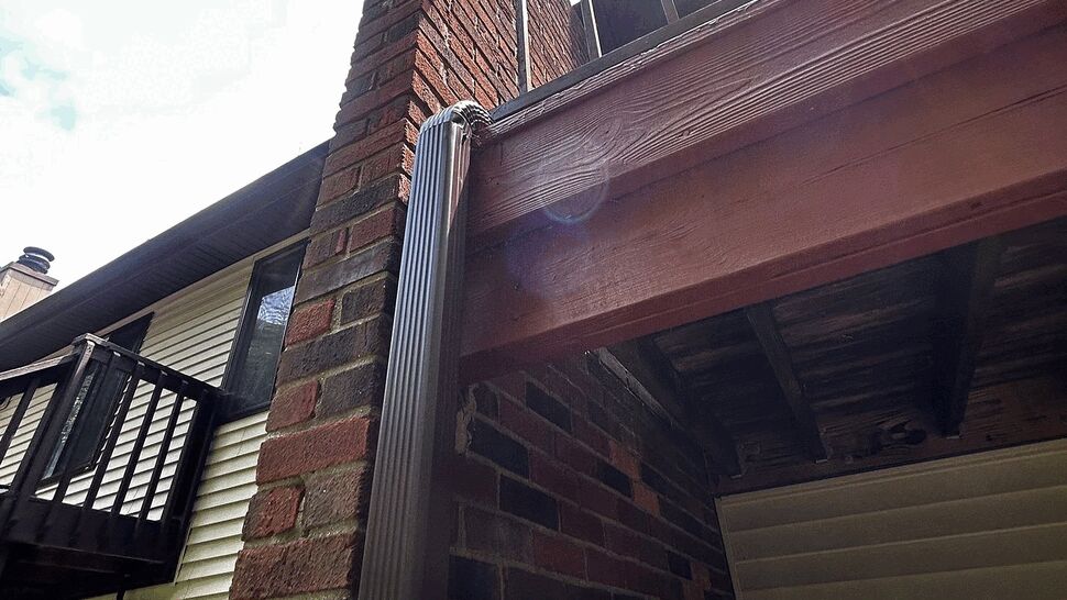 Brick chimney with vertical downspout and balcony railing above.