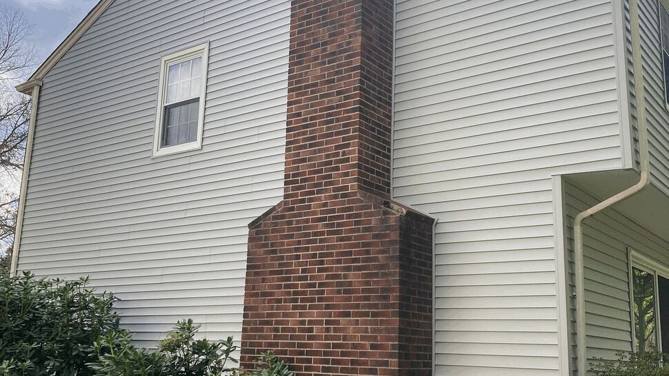 Brick chimney next to white vinyl siding and shrubs