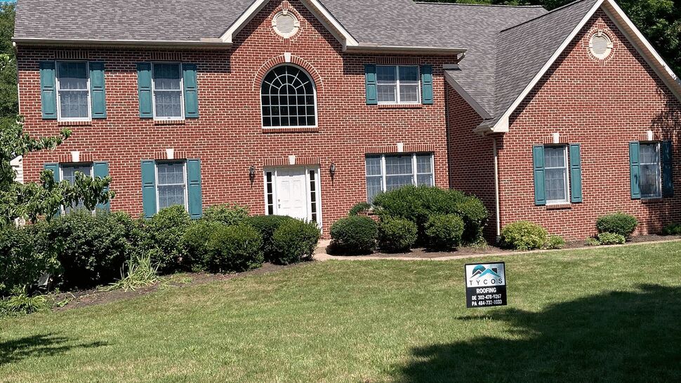 Two-story brick colonial home with gray roof and Tycos sign on the front lawn