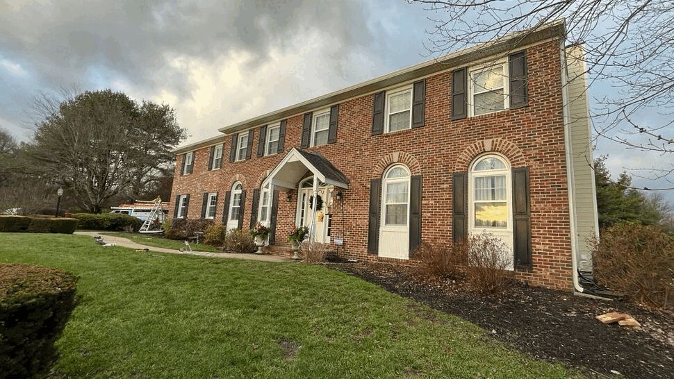 Two-story brick colonial home with dark roof and manicured lawn