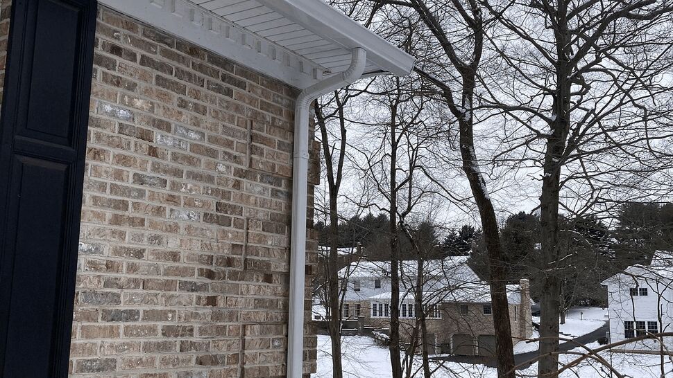 Brick house corner with white soffit and a white gutter downspout