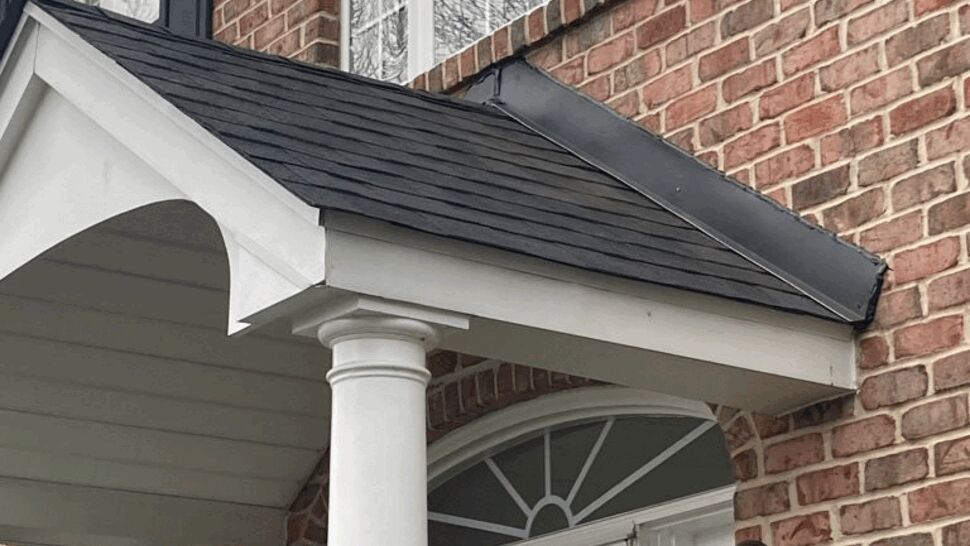 Close-up of brick entry with small shingled porch roof, white column, and lanterns
