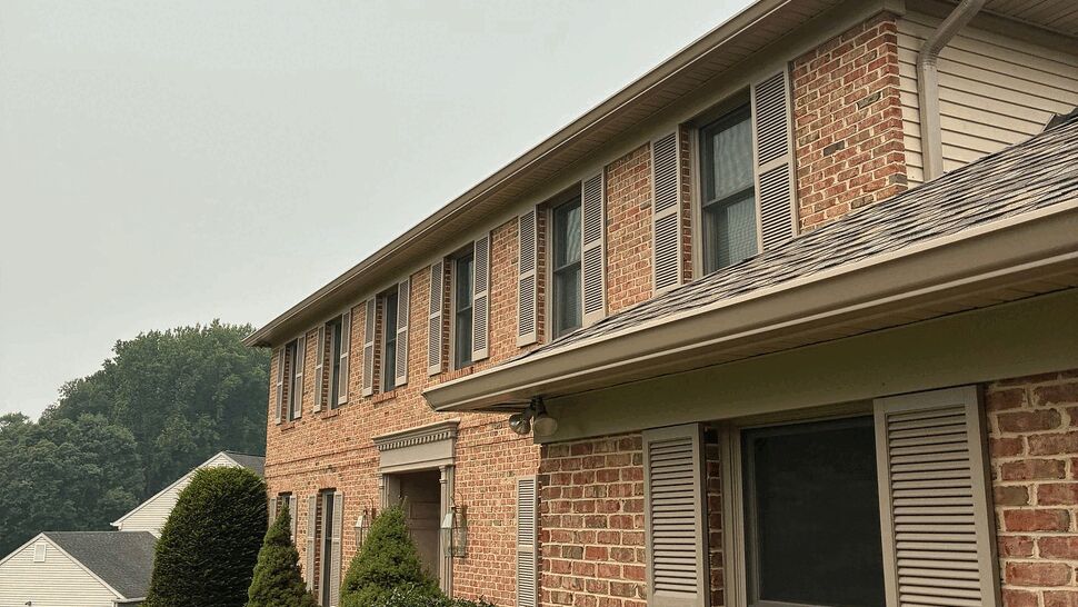 Side view of a brick facade showing gutters, shutters and upper windows.