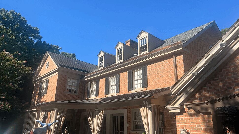 Brick colonial home with covered patio, curtains and outdoor seating under clear blue sky