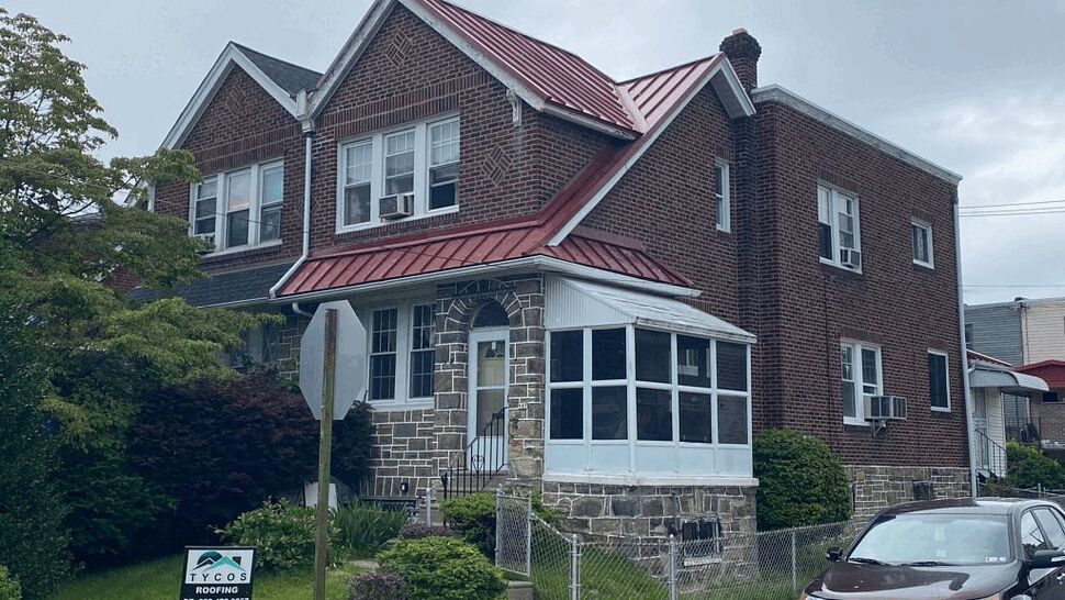 Front View Brick Home With Red Roof | Tycos Roofing And Siding Inc Two-story brick home with red metal roof and Tycos sign in front yard