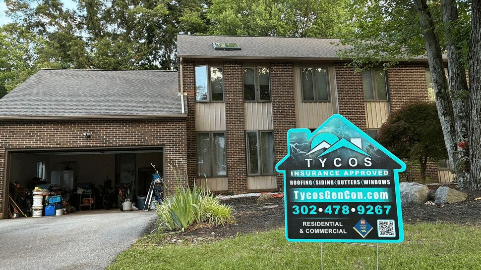 Two-story brick home with a Tycos yard sign on the lawn near the driveway