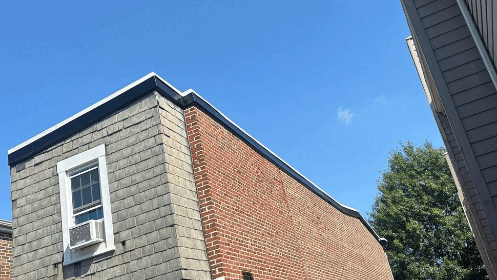 Backyard view of a brick rowhouse with shingle siding and window air conditioner