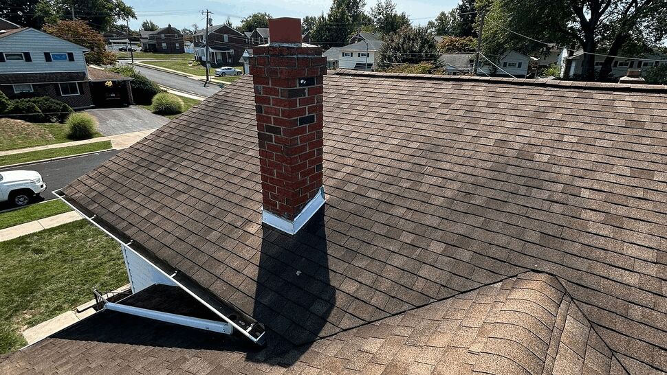 Brown shingle roof with red brick chimney under a clear sky.