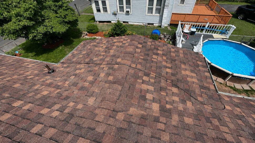 Aerial close-up of a brown asphalt shingle roof overlooking a backyard pool.