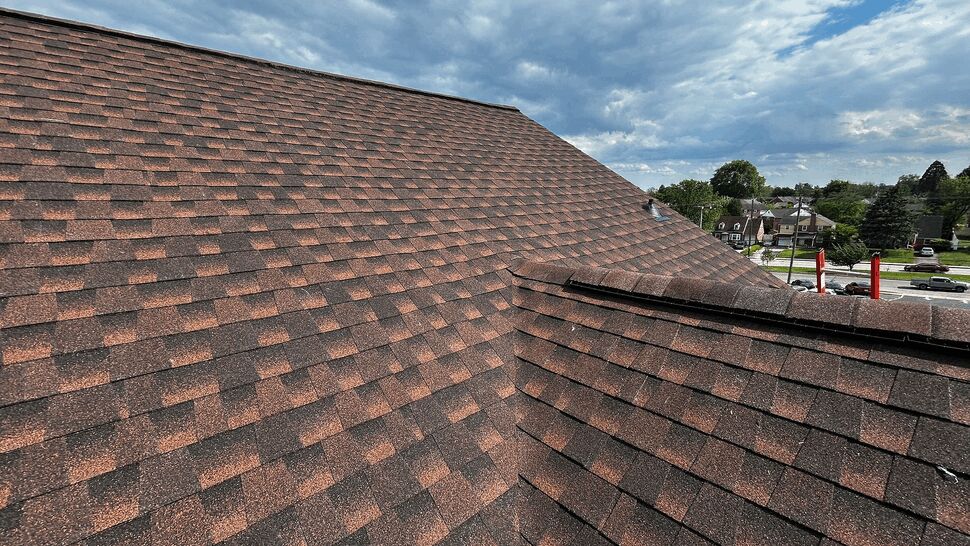 Close-up of brown asphalt shingle roof under a partly cloudy sky