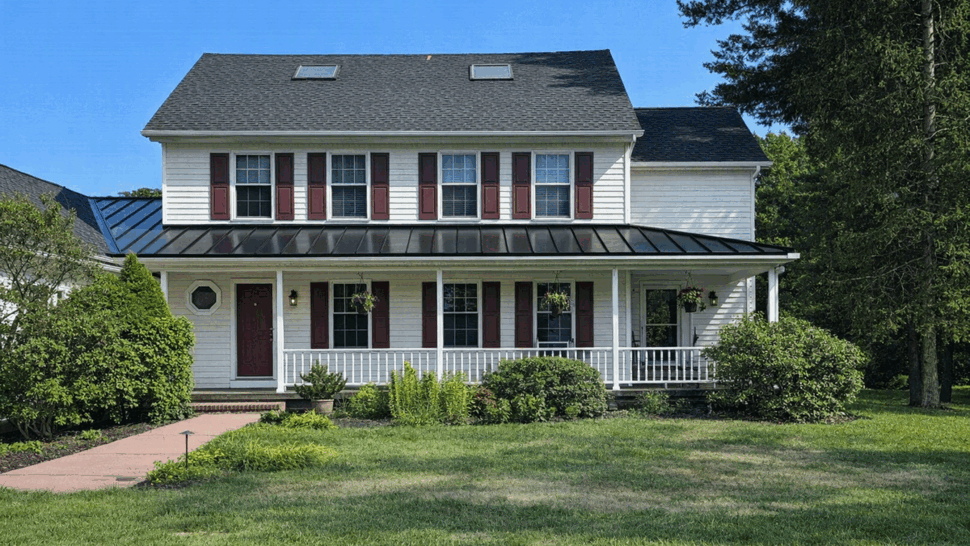 Front view of a colonial home with a black metal porch roof and asphalt upper roof