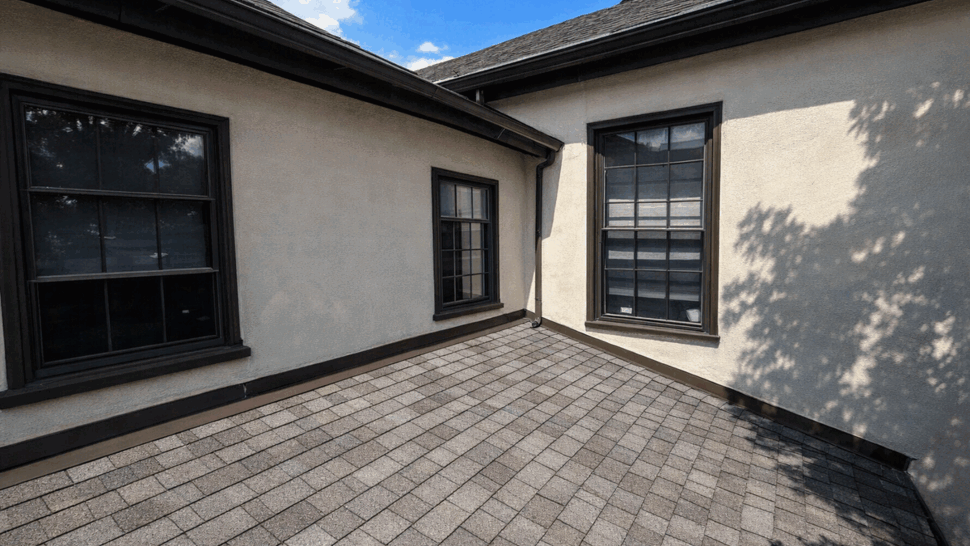 Flat dormer roof with asphalt shingles and two windows under a blue sky
