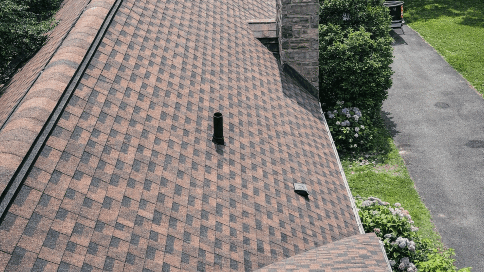 Roofline and stone chimney with patterned asphalt shingles.