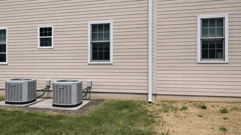 Vinyl siding and gutters on side elevation | Tycos Roofing And Siding Inc Side view of beige vinyl siding with gutters and two air conditioning units