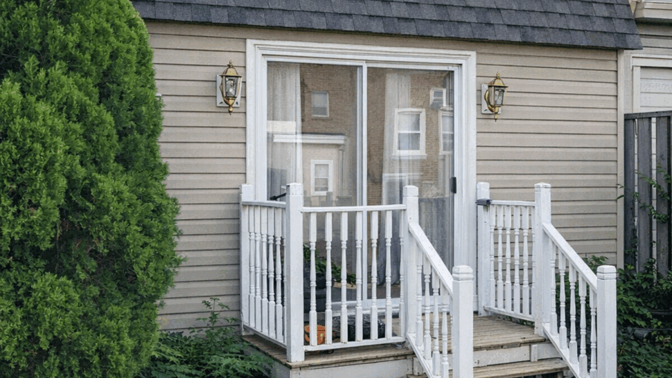 Small rear porch with vinyl siding, sliding door, white railing and trash bin
