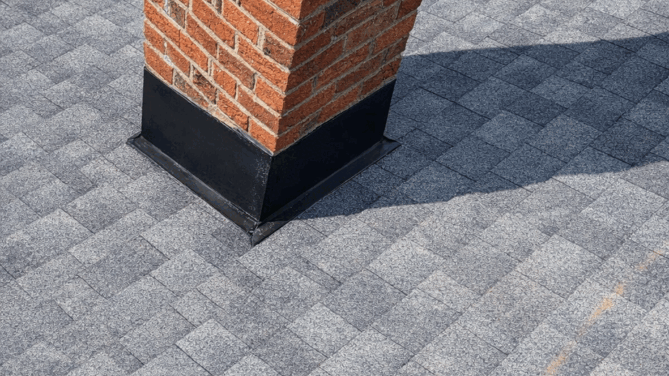 Brick chimney with new black metal flashing on shingles.