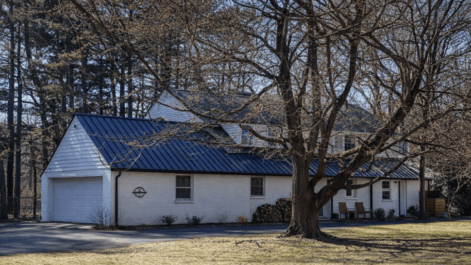 Side view of garage with black metal roof, gutters, and large tree in front.