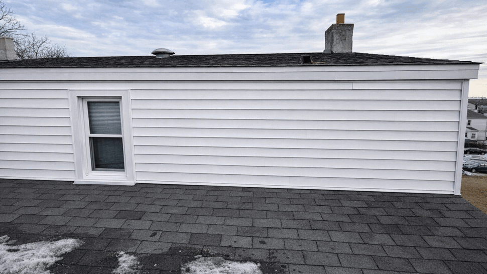 Gray asphalt shingle roof meeting white vinyl siding with a single window