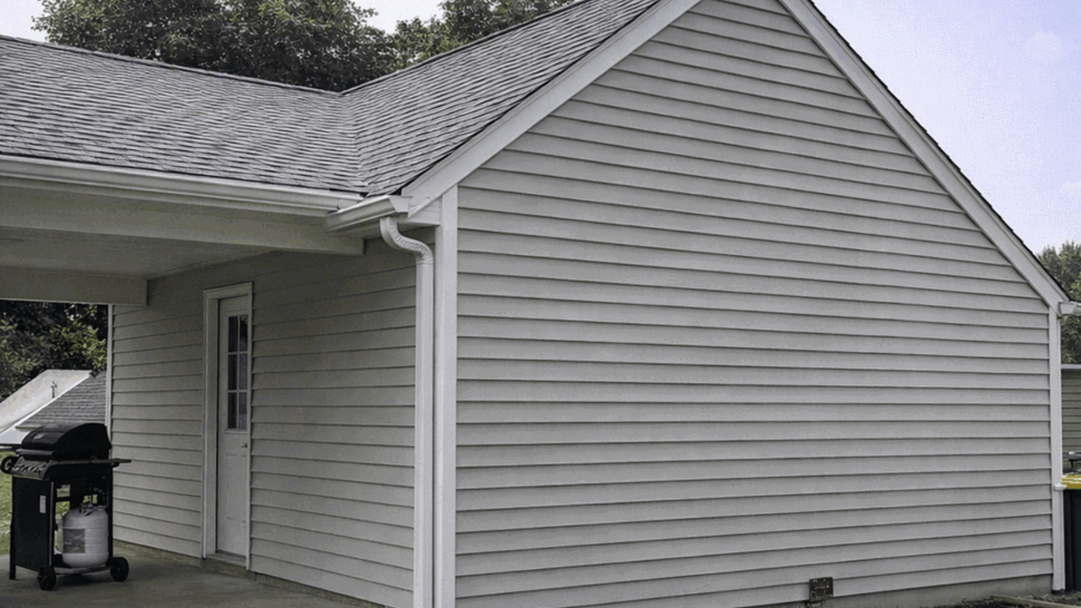 Gable end with white vinyl siding, shingled roof and corner gutter.