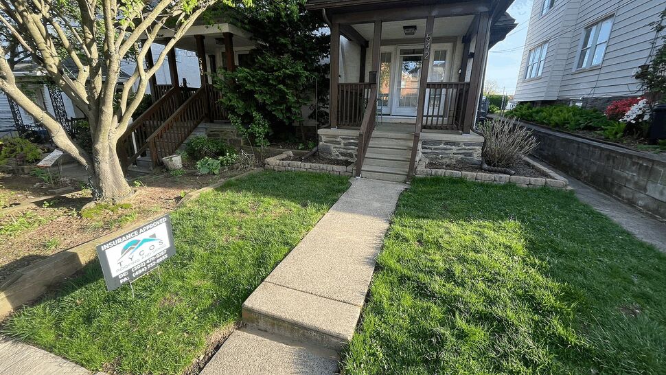 Covered front porch, sidewalk, and Tycos yard sign on a green lawn