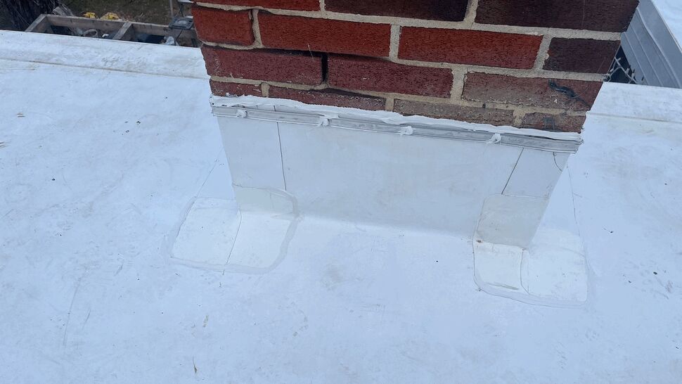 Close-up of patched chimney base flashing on white roof membrane