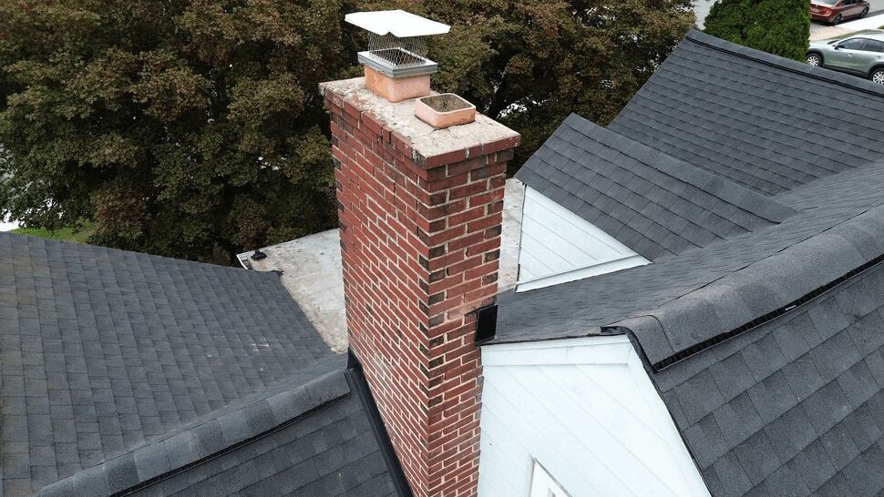 Brick chimney with metal flashing and shingled roof valley detail.
