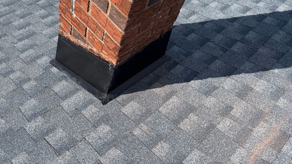 Brick chimney with new black metal flashing on shingles.