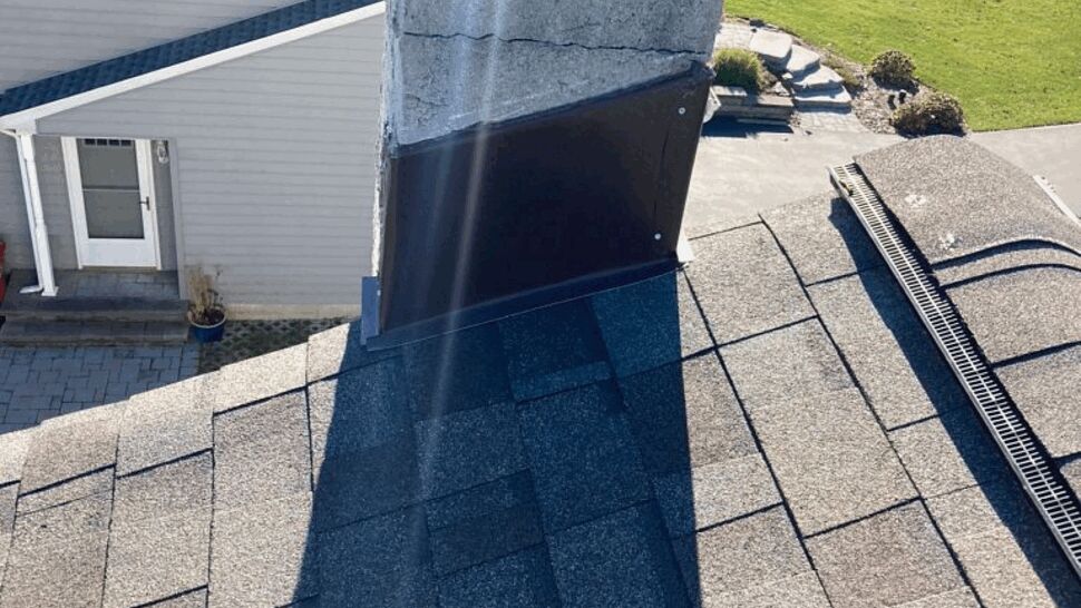 Close-up of chimney base with metal flashing and asphalt shingles on roof.