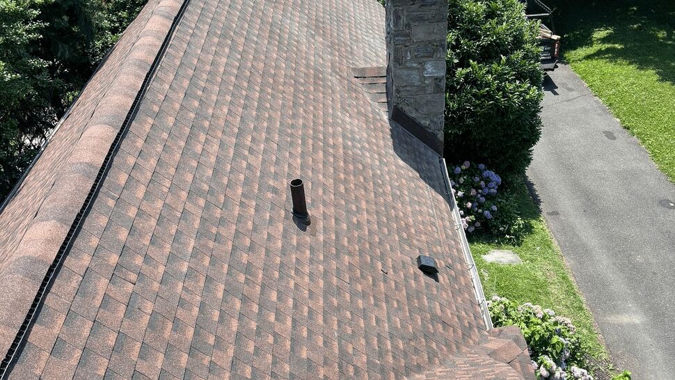 Roofline and stone chimney with patterned asphalt shingles.