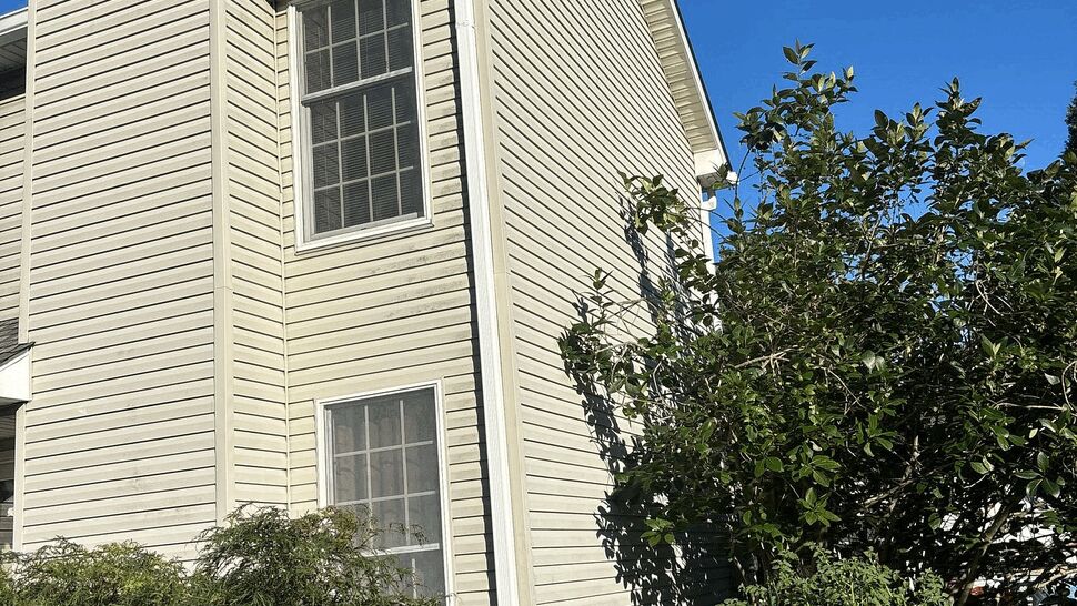 Two-story siding and chimney with windows and surrounding shrubs visible.