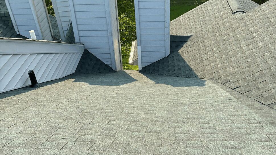Asphalt shingle roof with four white chimneys and a center roof valley