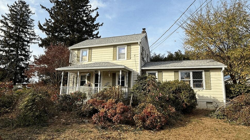 Two-story yellow house with porch, yard, and tall trees under a blue sky.