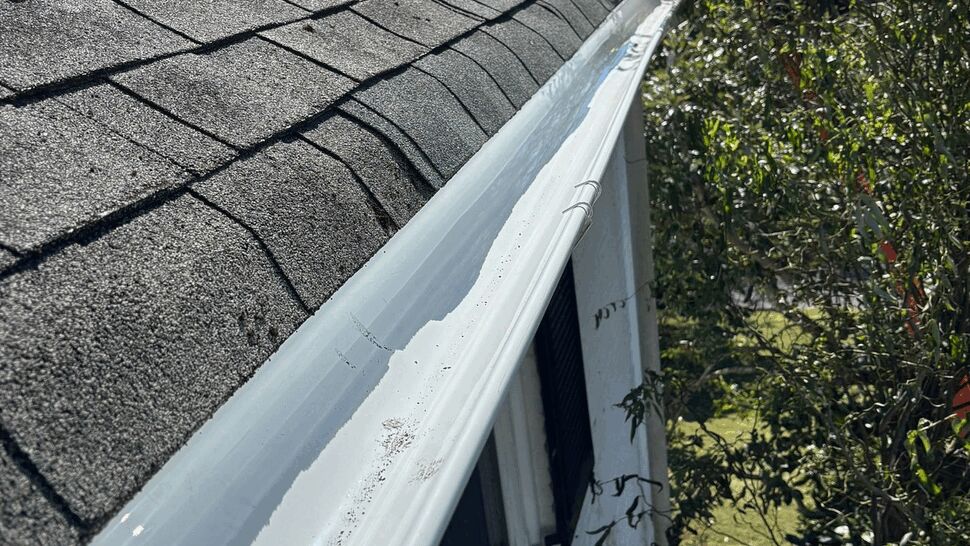 Close view of a white gutter running along an asphalt shingle roof