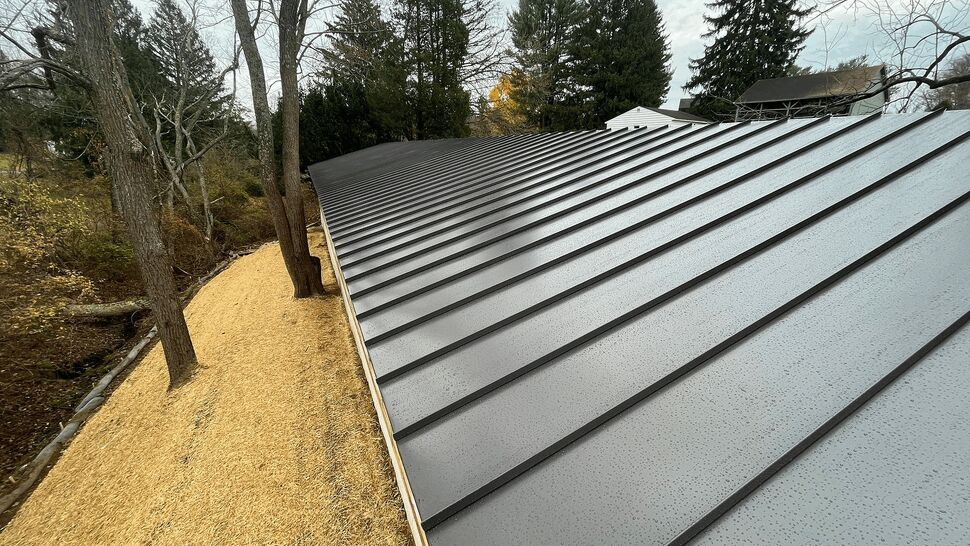 Close-up of dark standing-seam metal roof panels with raindrops.