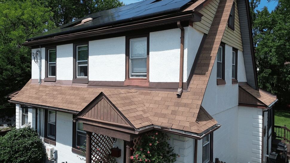 Close-up of brown shingle roof edge with gutter and second-story windows