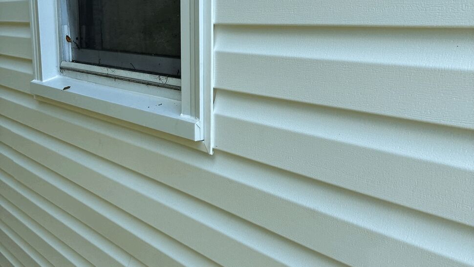Close-up of vinyl siding and window trim | Tycos Roofing And Siding Inc Close-up of white vinyl siding and window trim on exterior wall