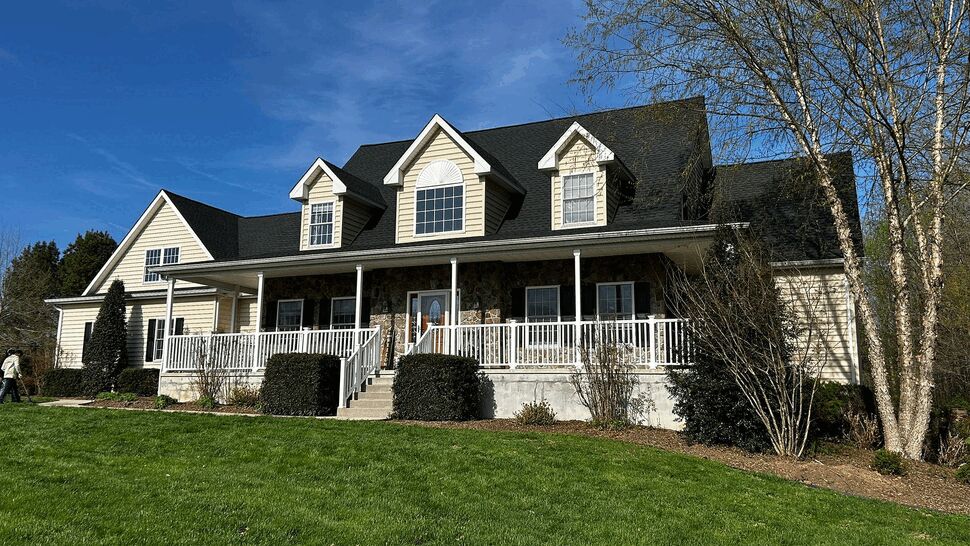 Large colonial home with black shingle roof, wraparound porch and beige siding