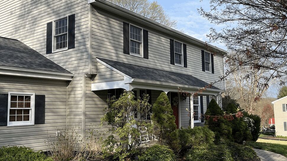 Two-story colonial house front with porch, beige siding, black shutters and a landscaped walkway.
