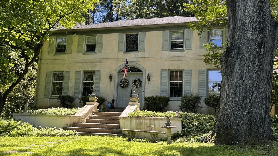 Front exterior of two-story colonial home with stucco siding and trees
