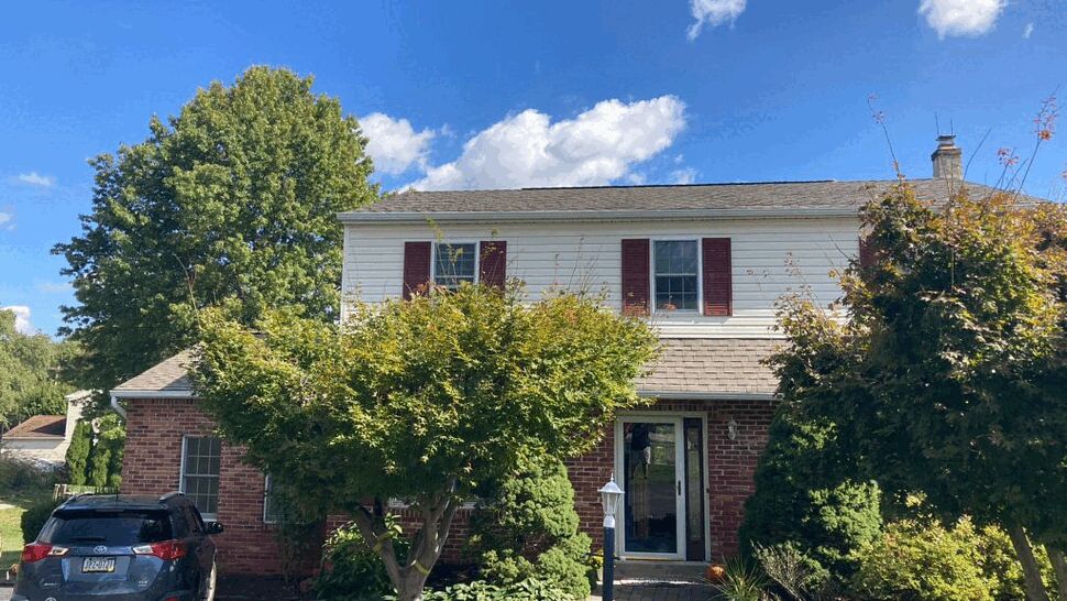 Two-story colonial house front with white siding, brick first floor, landscaping and driveway.