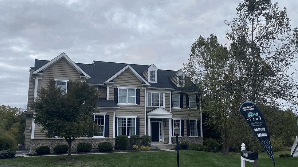 Two-story colonial home with a dark roof and a Tycos sign on the front lawn.