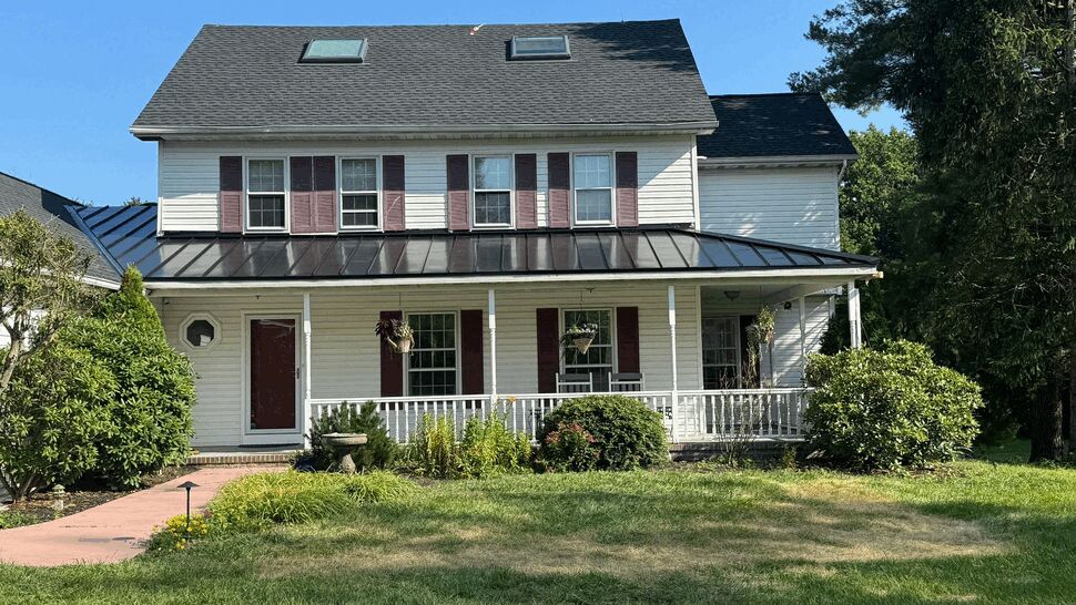 Front view of a colonial home with a black metal porch roof and asphalt upper roof