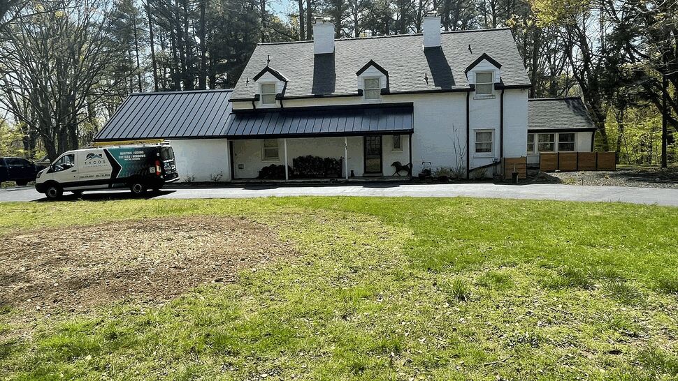 White colonial home with black standing seam metal roof and company van in driveway.
