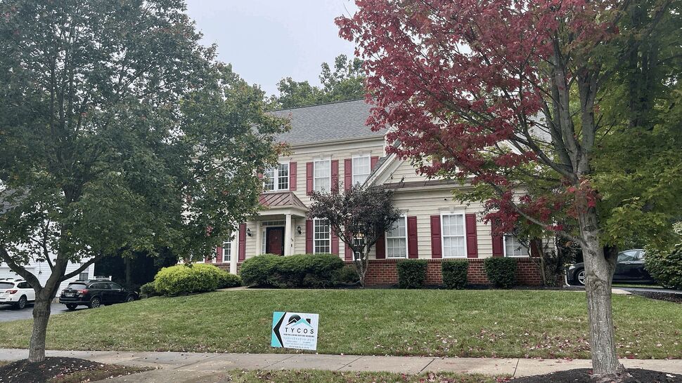 Front view of a colonial house with a Tycos sign on the lawn and a repaired roof