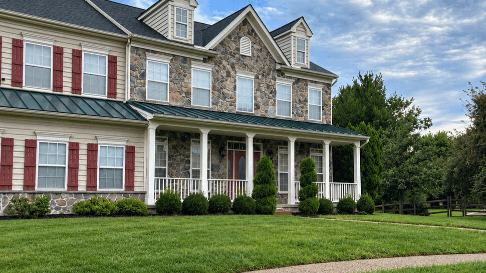 Two-story colonial home with dark shingle roof, stone and vinyl siding, white porch and red shutters