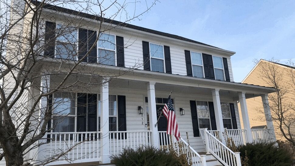 Two-story white house with front porch, black shutters and an American flag